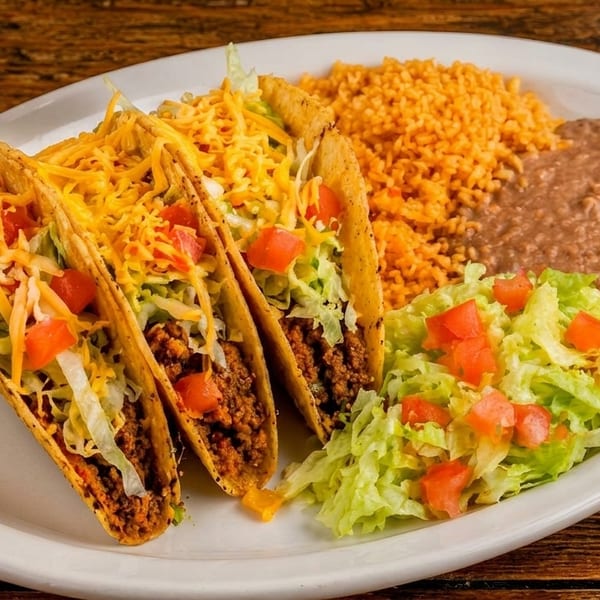 Three hard-shell tacos with ground beef, cheese, lettuce, and tomatoes, served with rice, beans, and salad.
